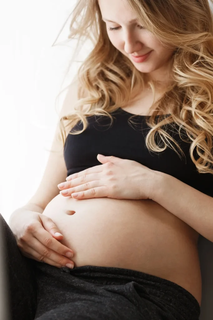 Kobieta w czarnym topie, która wie kiedy ma dni płodne, trzyma dłonie na swoim brzuchu.